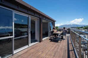 A deck with a wooden floor and glass doors leading to an interior space, overlooking a mountainous landscape. - The Brownston Hostel (Wanaka)