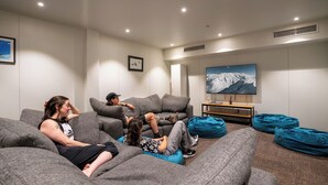 A modern living room with grey sofas, a flat-screen TV, and a large painting of a mountain landscape. - The Brownston Hostel (Wanaka)