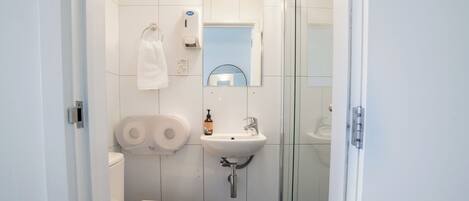 Un baño moderno con inodoro, lavamanos y cabina de ducha de vidrio.