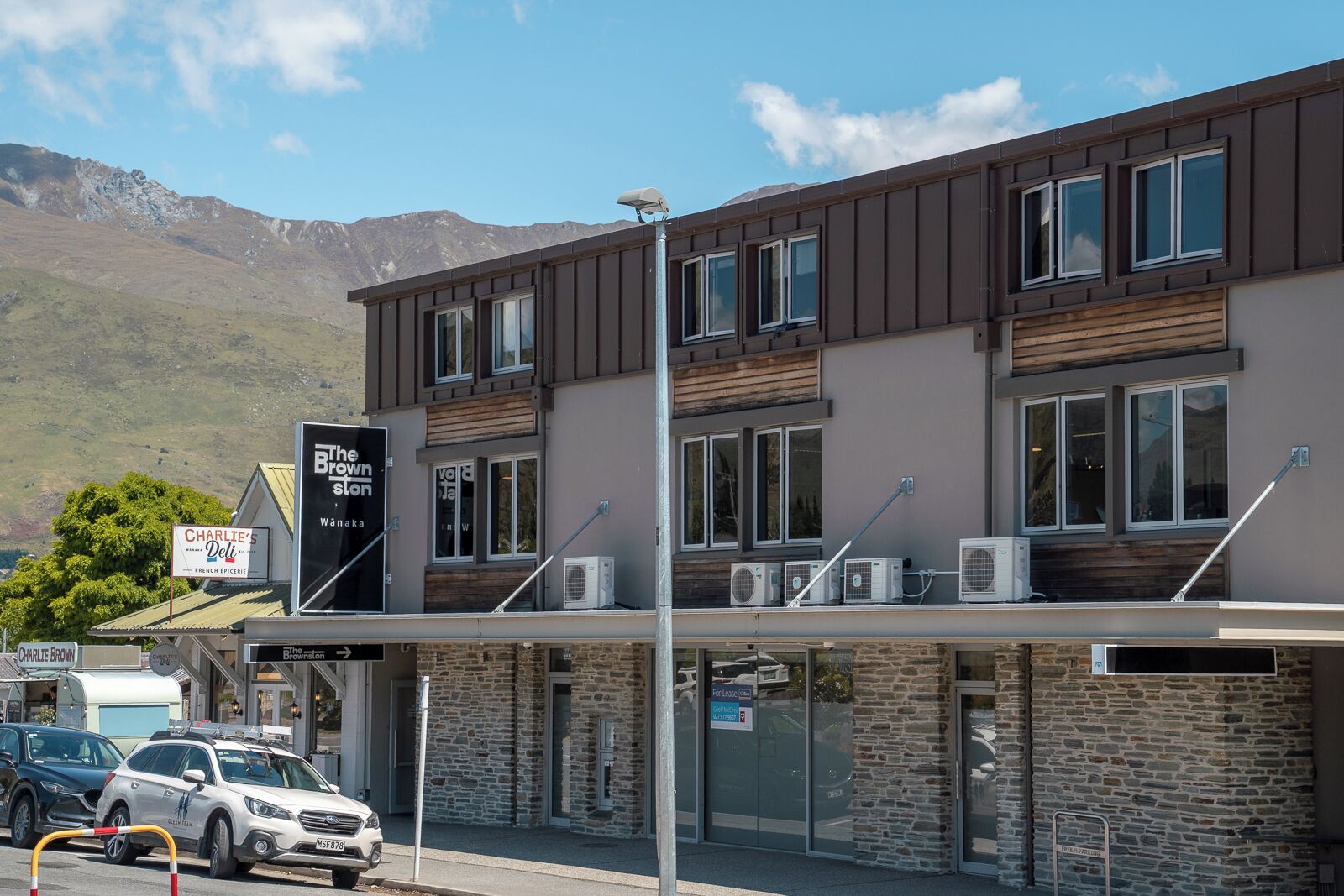 Un immeuble de deux étages avec une enseigne indiquant « The Brownston » et « Charlie Brown's Deli ». On voit des voitures garées et une montagne en arrière-plan.