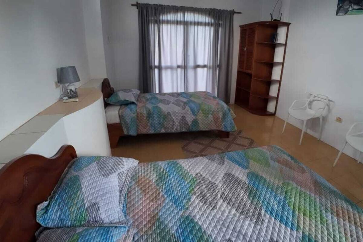 A bedroom with two beds, a desk, a chair, a wardrobe, and a window with curtains.