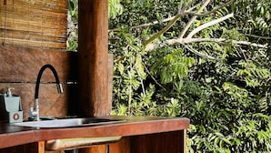 A wooden outdoor kitchen with a built-in sink, a hanging faucet, and a basket. - Casa da Mata Corumbau (Prado)