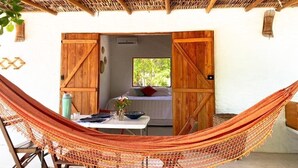 A hammock set up in a room with a thatched roof, wooden doors, and a view of greenery outside. - Casa da Mata Corumbau (Prado)