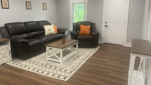 A living room with a dark leather sofa, a matching armchair, a wooden coffee table, and a patterned rug.
