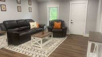 Un salon avec un canapé en cuir foncé, un fauteuil assorti, une table basse en bois et un tapis à motifs.