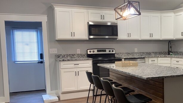 A modern kitchen with white cabinets, a granite countertop, a stainless steel microwave, a built-in oven, and a bar stool area.
