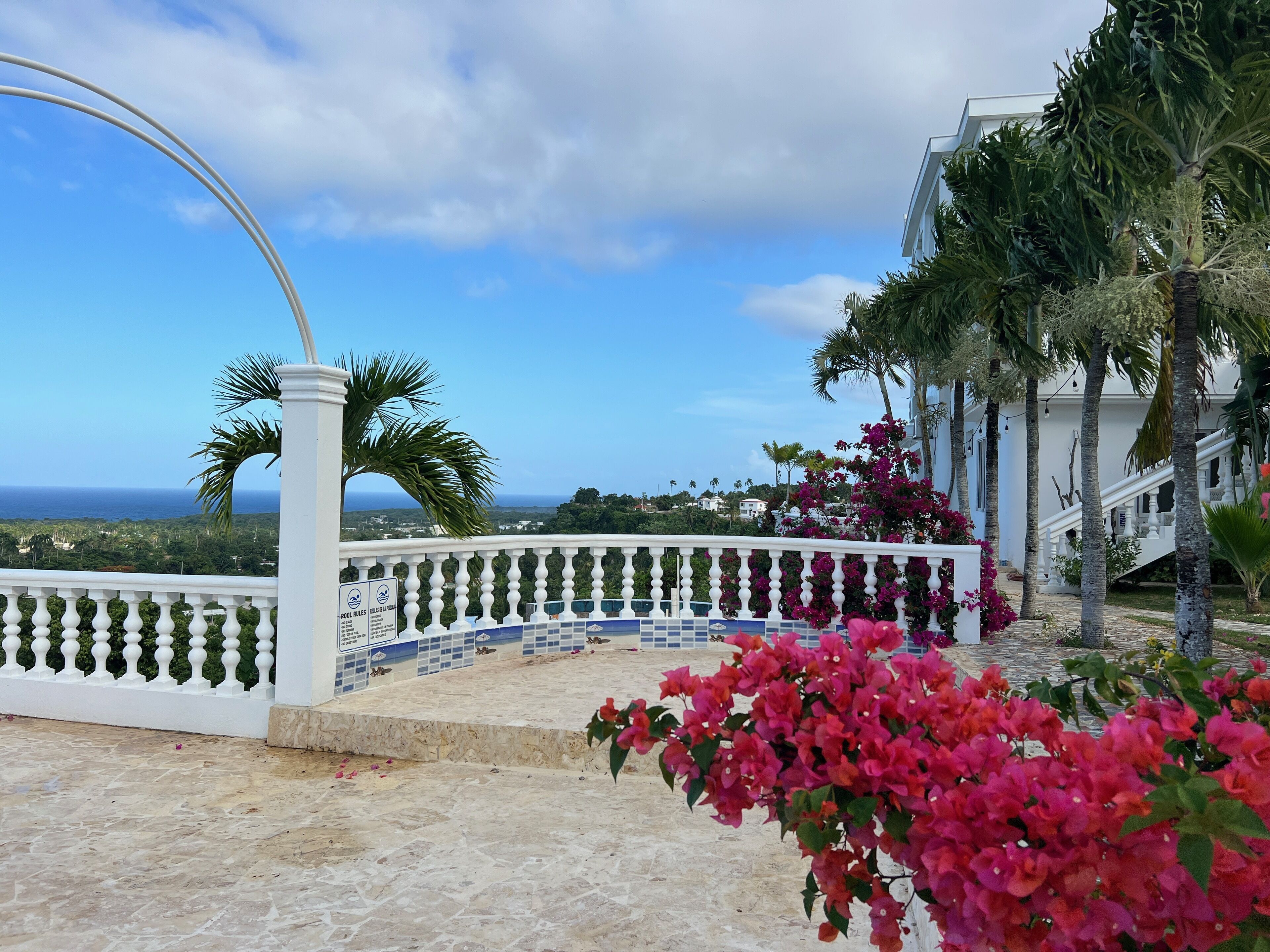 Een balkon met uitzicht op zee, een wit hekwerk en bougainvillea bloemen.