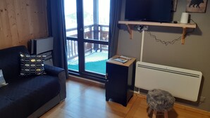 A cozy living room with a sofa, a small table, a TV on a stand, and a view of a snowy deck outside. - Studio Cosy Les Deux Alpes Centre (Les Deux Alpes)