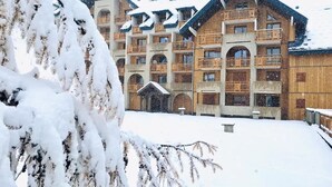 A multi-story building with balconies, a covered entrance, and snow-covered surroundings. - Studio Cosy Les Deux Alpes Centre (Les Deux Alpes)