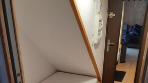 A small, compact room with a foldable bed, a wooden floor, a white wall, and a door leading to another room. - Studio Cosy Les Deux Alpes Centre (Les Deux Alpes)