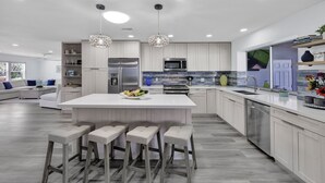 A modern kitchen with a central island, bar stools, stainless steel appliances, and pendant lighting. - Spacious beach home - Sleeps 12 - Steps from dining, with a private heated pool (Marco Island)