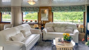 Une pièce chaleureuse avec deux canapés en cuir blanc, une petite table basse ronde et une vue sur un étang, visible à travers de grandes fenêtres.