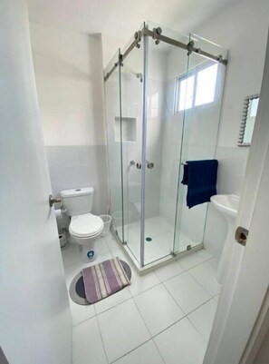 Modern bathroom with a glass-enclosed shower, white toilet, and clean tiled flooring.