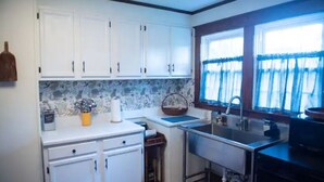 Una cocina compacta con armarios blancos, un lavamanos integrado y un ventanal con cortinas azules.