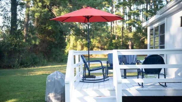 Una terraza techada con mobiliario exterior, una parrilla y un paraguas rojo.