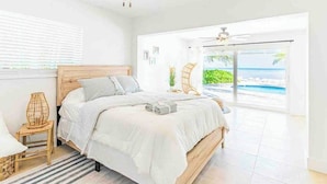 Un dormitorio con cama, mesita de noche, lámpara, vista a la playa y ventilador de techo.