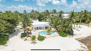 Una propiedad frente a la playa con piscina, palmeras y un edificio blanco.