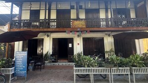 A traditional building with a balcony, a signboard for Khost Guesthouse, and a bus ticket sign listing destinations.
