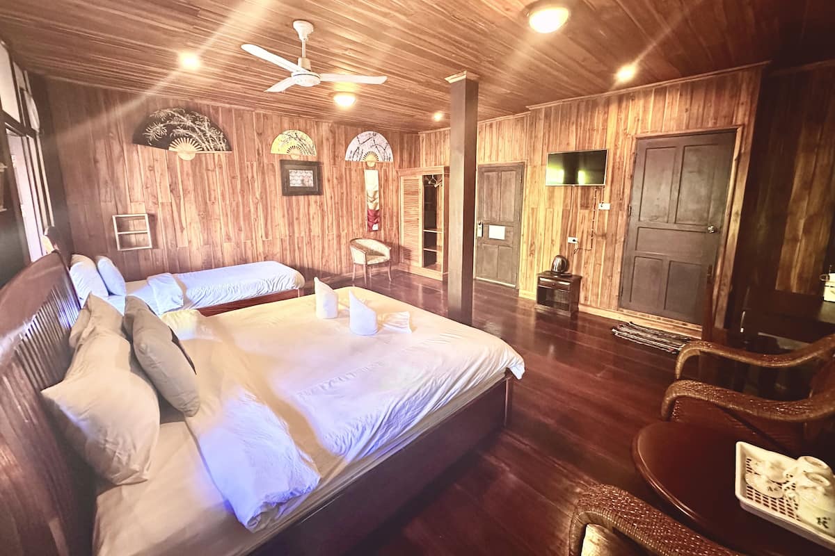 A wooden-paneled room with a large bed, a chair, a TV, and a door.