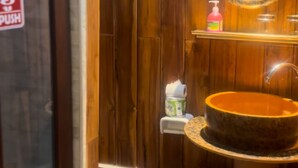 A bathroom with wooden walls, a round mirror, a sink, and a trash bin.