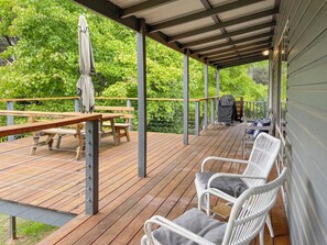 A wooden deck with picnic tables and white wicker chairs, surrounded by greenery. - Tranquil Holiday house in Kevington (Kevington)