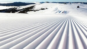 Ein schneebedeckter Skipistenhang bei blauem Himmel.