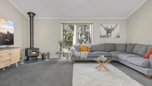 Ein modernes Wohnzimmer mit grauem Sofa, weißem Teppich, Couchtisch aus Holz und einem schwarzen Kaminofen.