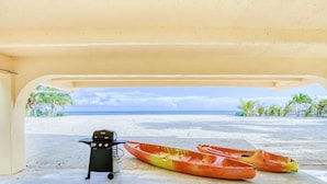 A beach view from a covered area with a grill and kayaks.