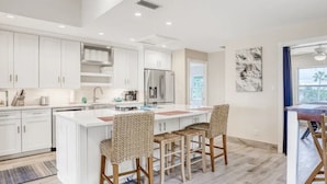 A modern kitchen with white cabinetry, a central island with bar stools, stainless steel appliances, and a view of the outdoors.
