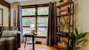 Une pièce confortable avec un canapé, une petite table avec une lampe, une bibliothèque et une grande fenêtre avec des rideaux.