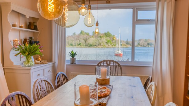 A dining table with candles, chairs, and a view of the sea through a window. - Eigionfa -  an on the beach that sleeps 8 guests  in 3 bedrooms (Menai Bridge)