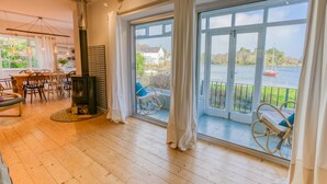 A spacious room with a large window overlooking a body of water, a wooden floor, and a seating area with chairs. - Eigionfa -  an on the beach that sleeps 8 guests  in 3 bedrooms (Menai Bridge)