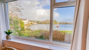 A view from a window overlooking a lake with a house and a sailboat. - Eigionfa -  an on the beach that sleeps 8 guests  in 3 bedrooms (Menai Bridge)