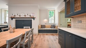 Een keuken met een houten tafel, stoelen, een bank met kussens en een wijnrek met onderscheidingen.
