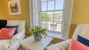 Una habitación con dos sofás a rayas, una mesita con un jarrón de tulipanes y una ventana con vistas a un edificio de piedra.