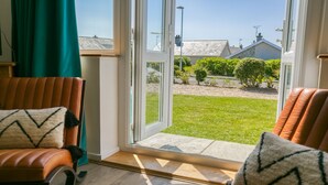 Una habitación con un gran ventanal corredero que da a un jardín. Hay dos sillones de cuero con cojines estampados.