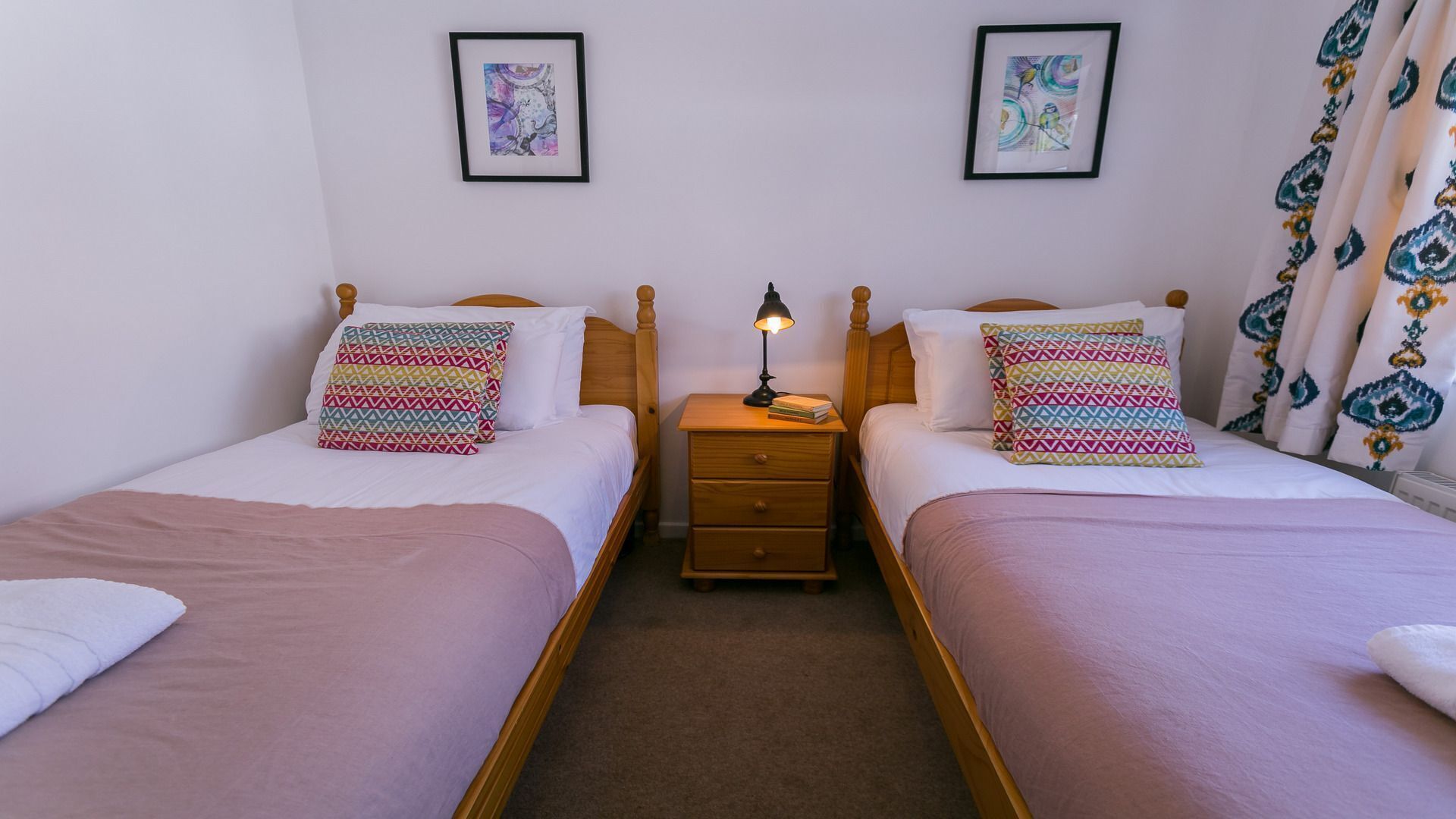 A double room with two beds, each with patterned pillows and a bedside table with a lamp.