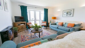 Una sala de estar con un sofá, un televisor, una mesa de centro con una planta y una alfombra estampada.