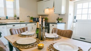 A dining area with a table set for two, featuring white plates, wine glasses, and candles. - Ty Melyn -  sleeps 4 guests  in 2 bedrooms (Beaumaris)