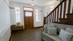 A hallway with a wooden door, a bench, a staircase, and a wall-mounted light fixture.