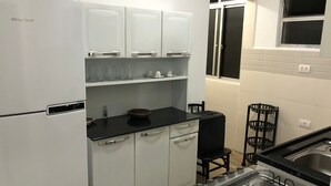 Cocina compacta con armarios blancos, encimera negra, estufa a gas y ventana con persianas.