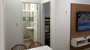 Habitación de hotel con zona de comedor, televisor montado en la pared y baño visible a través de una puerta abierta.