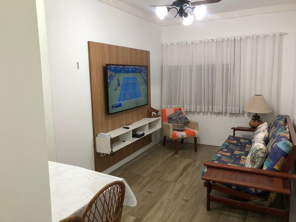Una sala de estar con un televisor montado en la pared, un sofá, una silla, una mesita y una lámpara.