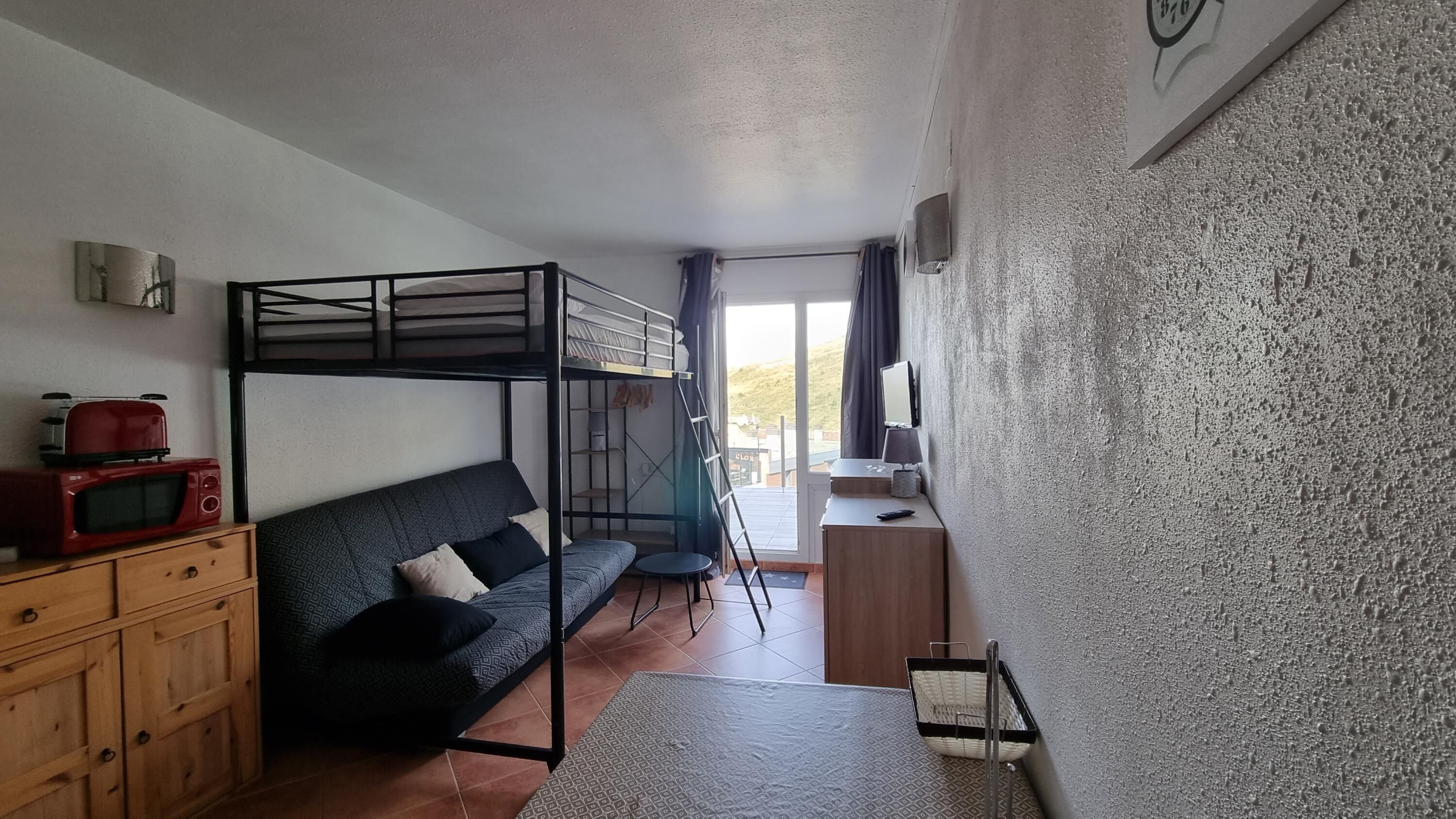 Une pièce compacte comprenant un lit superposé, un canapé, une petite table, un four à micro-ondes et une commode.