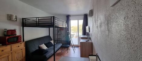 A compact room with a bunk bed, a sofa, a small table, a microwave, and a dresser.