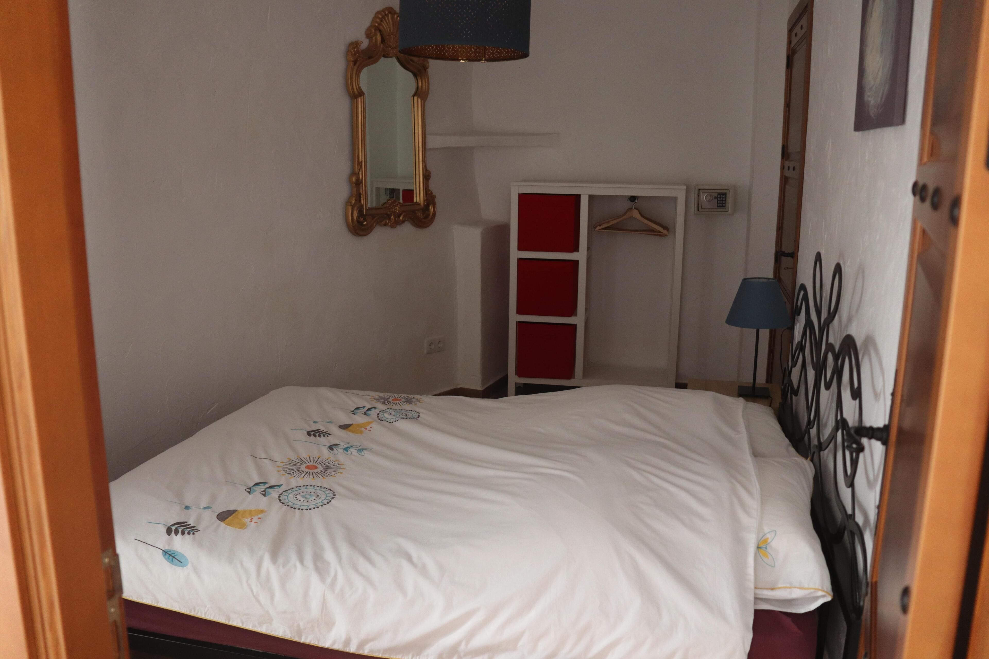 Un dormitorio con cama, armario, espejo y lámpara colgante.