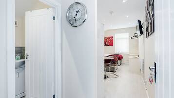 A modern kitchen with a white door, a wall-mounted clock, and a dining area with a red decorative piece.