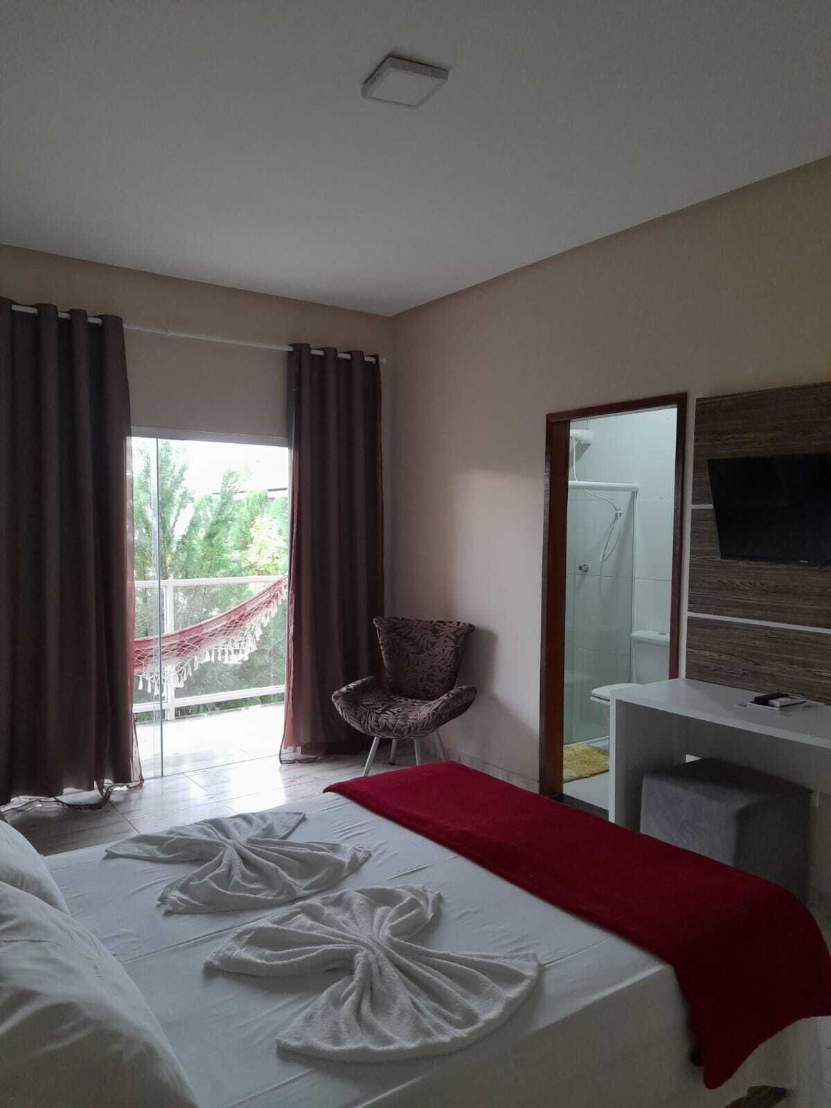 A hotel room with a bed, a chair, a desk, and a large window with curtains.