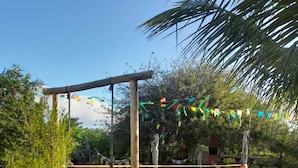 Un jardín con un conjunto de columpios de madera, una hamaca y banderas de colores.