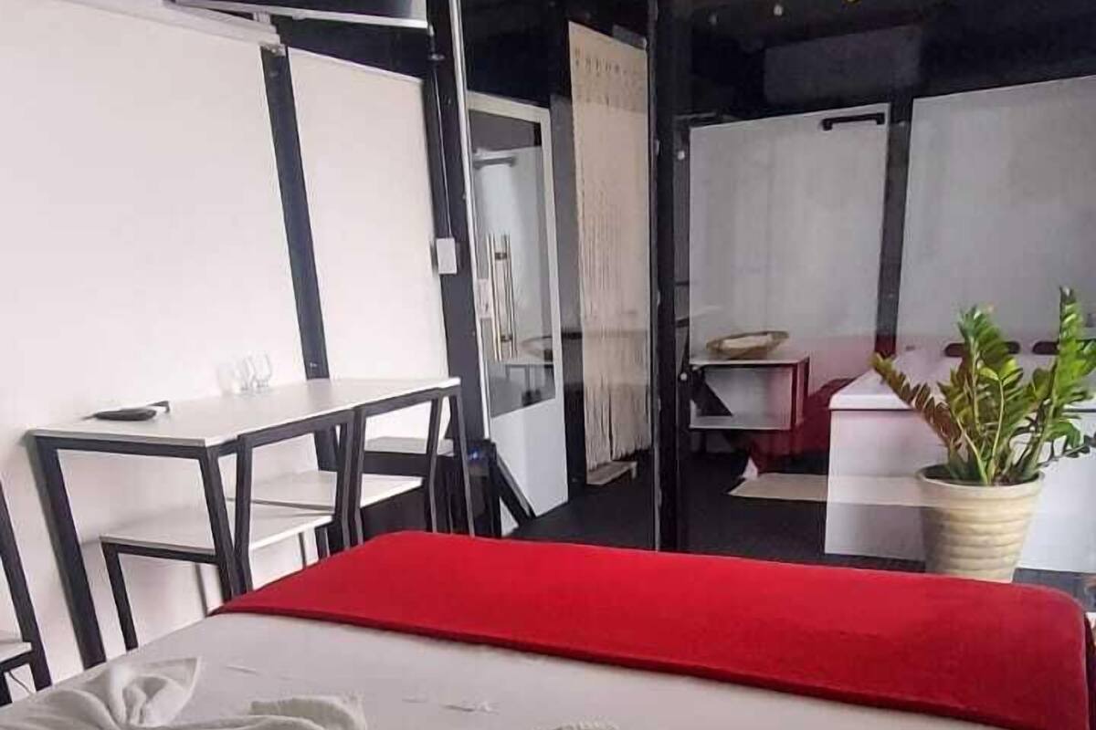 Ett hotellrum med en säng, ett litet bord, en stol, en krukväxt och en vägg som är accentfärgad i rött.